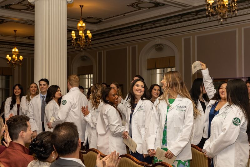 RUSH University White Coat Ceremony — students in white coats celebrating in a formal ballroom with guests applauding